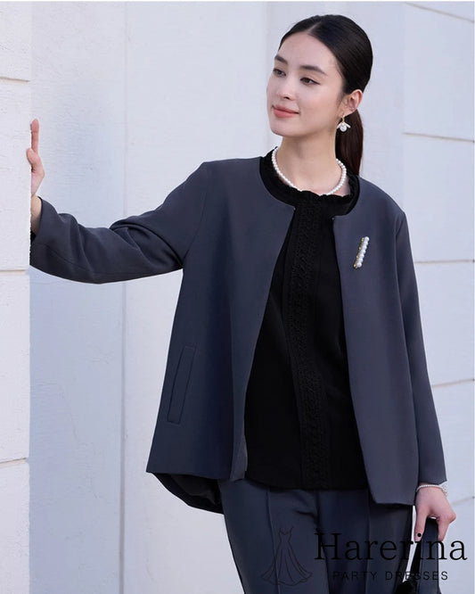 ノーカラージャケットとパンツのダークネイビーセットアップを着た女性モデルの上半身カット。黒トップスとパールアクセサリーを合わせた上品なスタイリング。