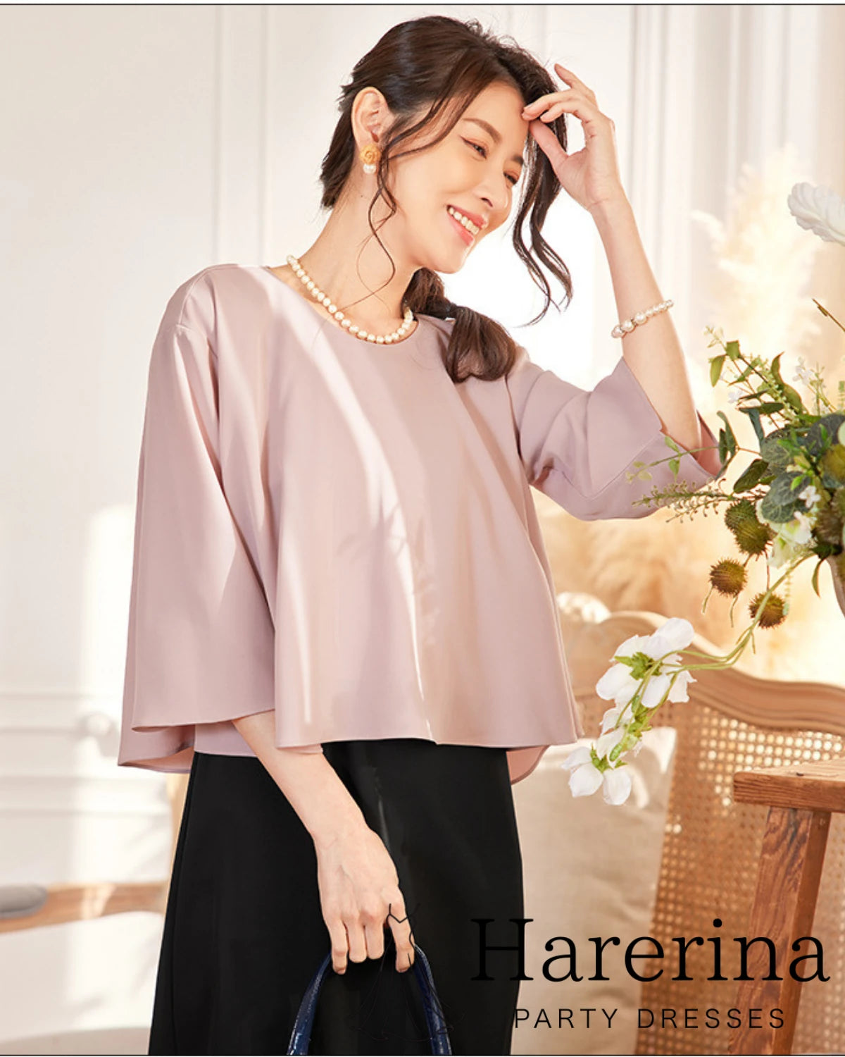 グレーパープルのケープ風トップスを着た女性モデルが微笑みながら花を持つコーディネート。上品な素材感と七分袖デザインが特徴のフォーマル3点セット。
