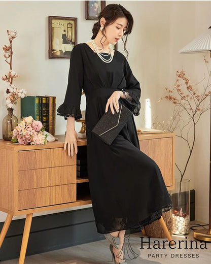 黒のレース袖×フレアロングワンピースを着た女性がキャビネットに寄りかかり、クラッチバッグを持って上品に佇むフォーマルコーデ写真。
