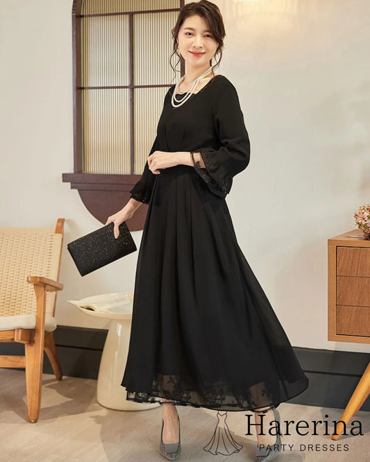 黒のレース袖×フレアロングワンピースを着た女性が横向きで優しく微笑みながらポーズをとるエレガントなスタイル写真。
