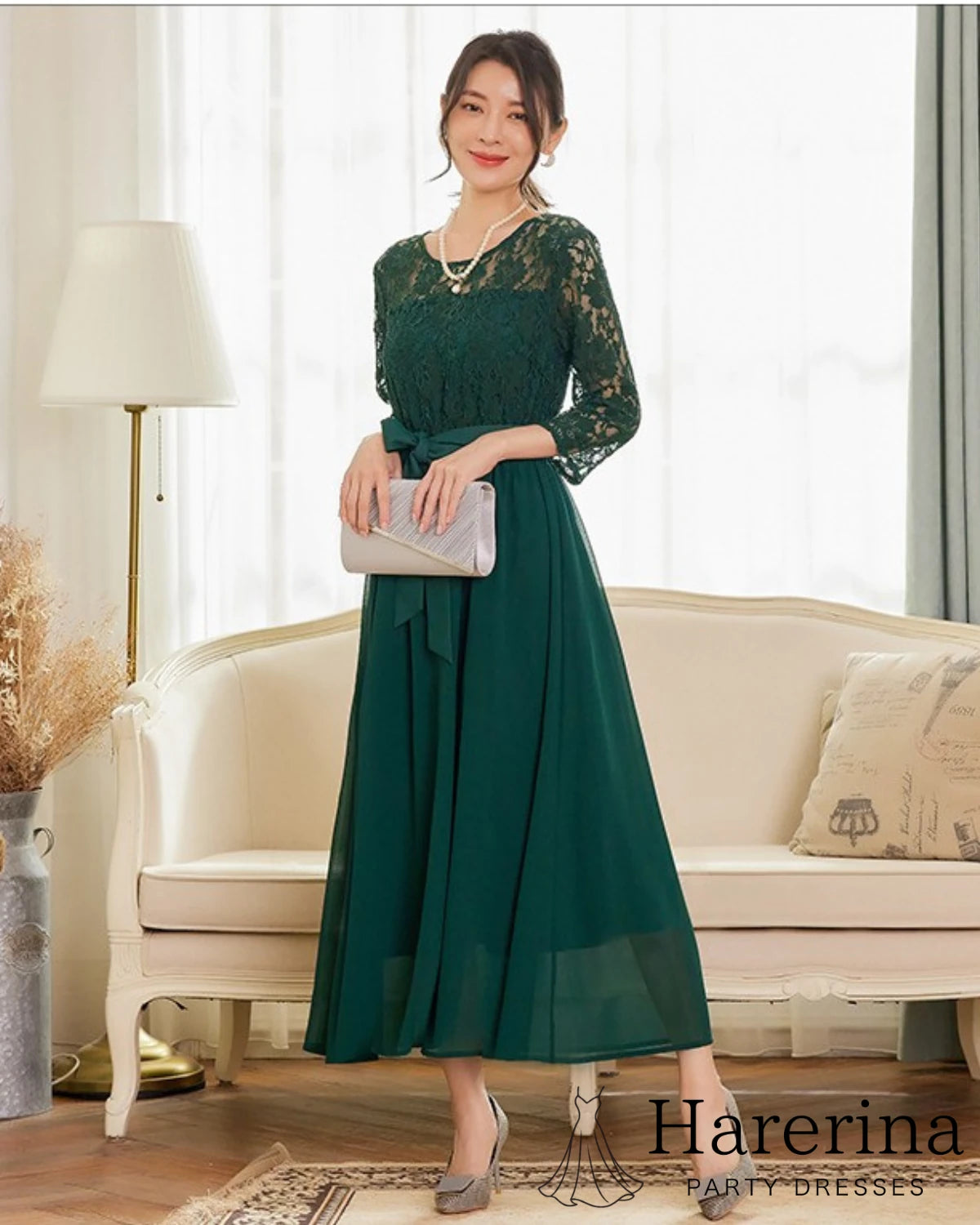 グリーンの七分袖レースワンピースを着用した女性の正面全身写真。ウエストリボンとシフォンスカートの軽やかな揺れが上品で、フォーマルシーンに映える装い。
