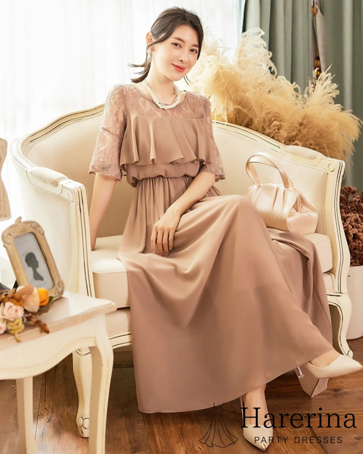 ブラウンのレーストップ×シフォンロングワンピースを着た女性が、ソファに座って穏やかに微笑むシーンの画像
