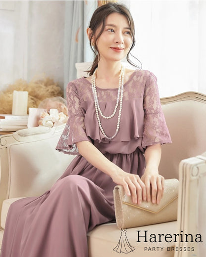 グレーパープルのレーストップ×エアリーシフォンロングワンピースを着た女性がソファに座り、クラッチバッグを持って微笑む様子の画像
