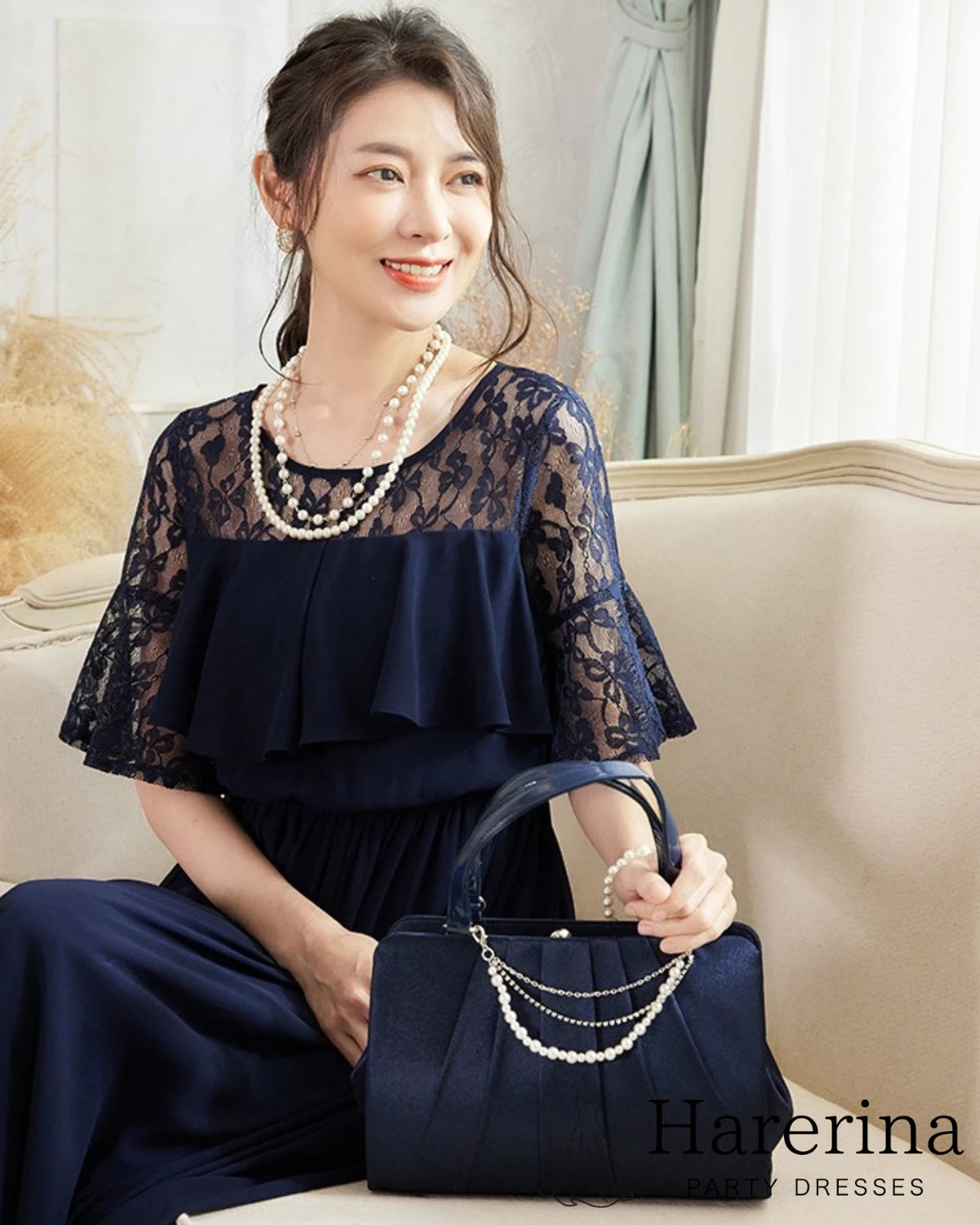 ネイビーのレーストップドレスを着た女性がソファに座って優しく微笑むアップショット
