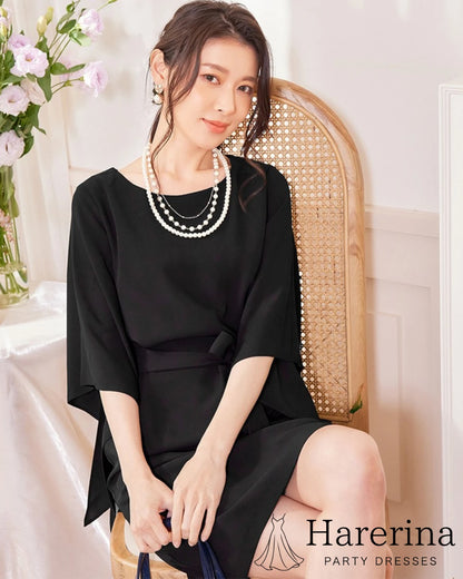 ブラックのフレアスリーブ×ウエストリボン風デザインワンピースを着た女性が椅子に座って上品に微笑む写真。
