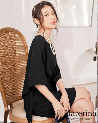 ブラックのフレアスリーブ×ウエストリボン風デザインワンピースを着た女性が椅子に座り横向きで視線を向けている写真。
