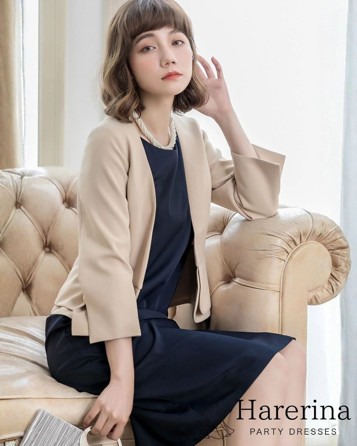 ベージュのペプラム風フォーマルジャケットを着用した女性がソファに座っている上品なショット

