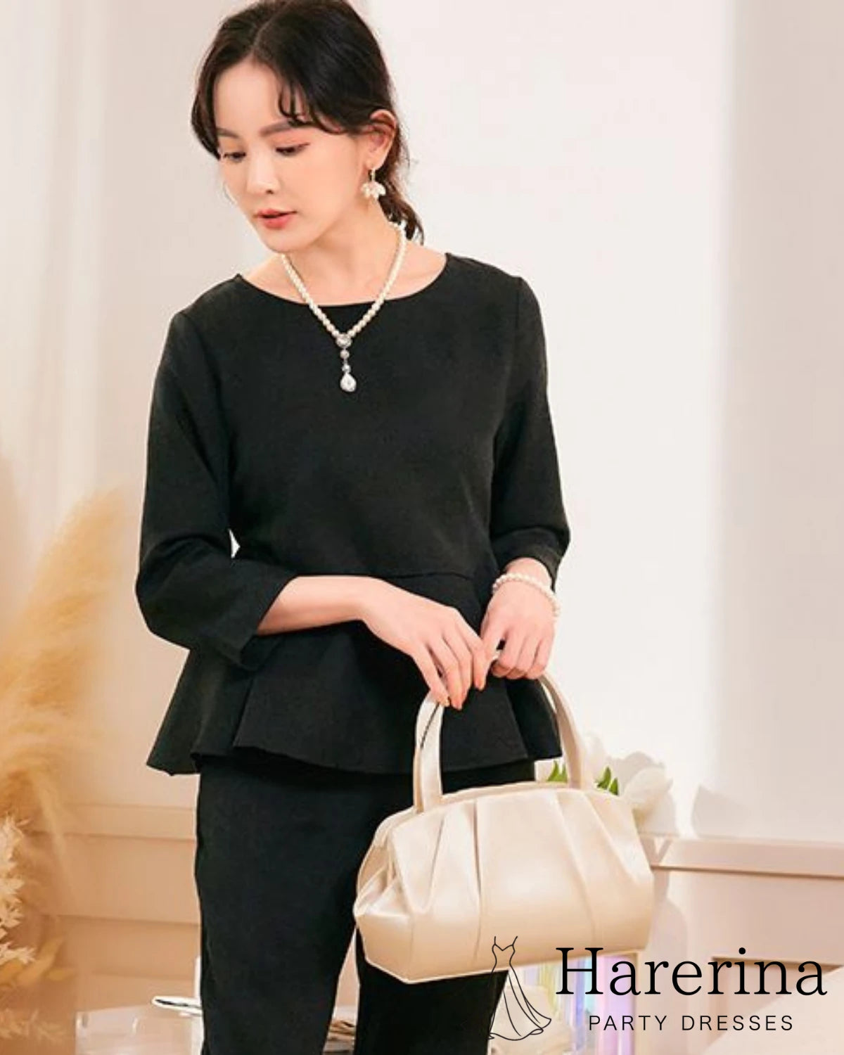 黒のトップスを着た女性がベージュのプリーツデザインパーティーバッグを手に持って立っている着用イメージ
