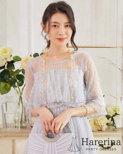グレーのレースケープロングドレスを着た女性が上品に立っている上半身アップ写真
