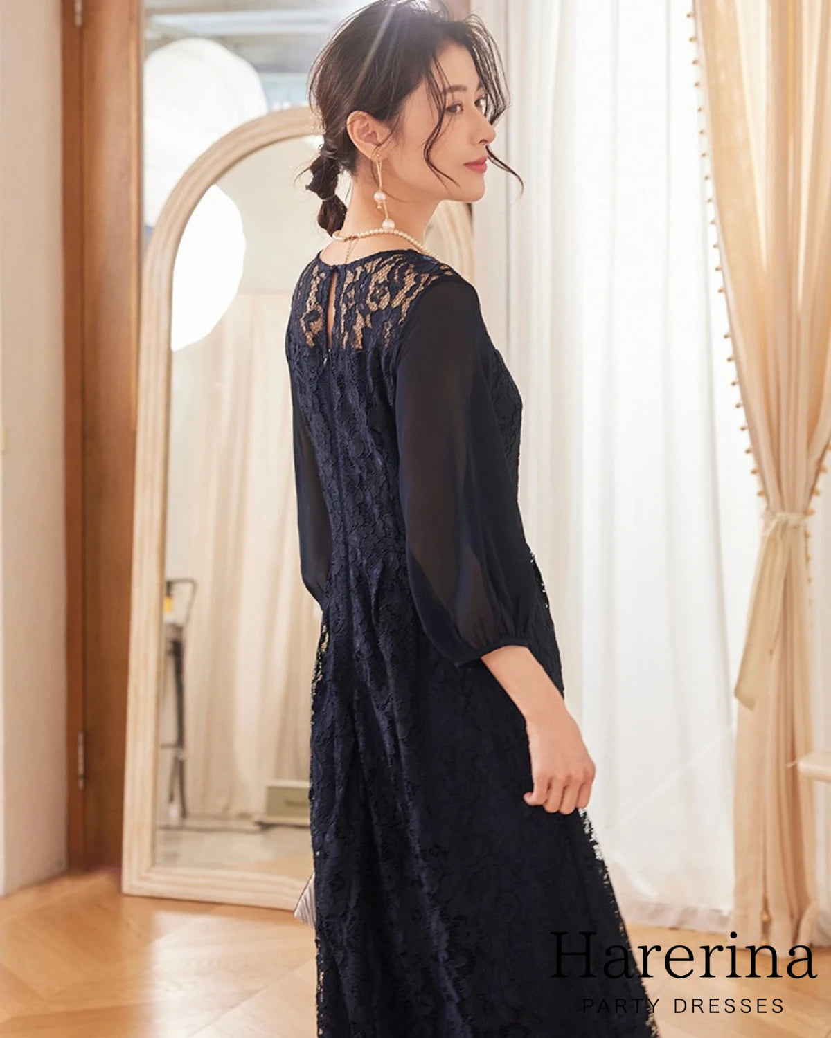 上品レース×シフォン袖ロングワンピースのネイビーを着用した女性が後ろ向きで振り返る姿。背中のレース切り替えとシフォン袖が上品に映る商品イメージ写真。
