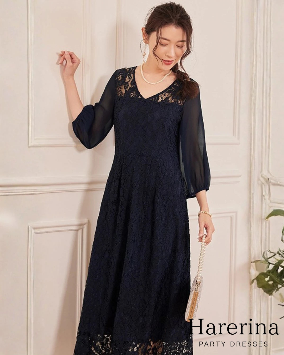 上品レース×シフォン袖ロングワンピースのネイビーを着用した女性が下を向いて立つ姿。レースのVネックとシフォン袖、ロング丈ラインが上品に映える商品イメージ写真。
