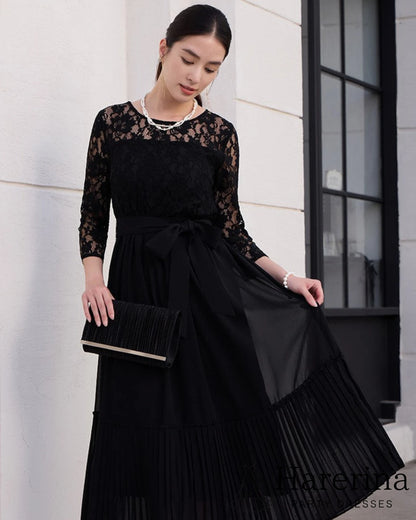ブラックのレースシフォンドレスを着た女性が黒いクラッチバッグを持ちスカートを軽く広げる上半身寄りのショット
