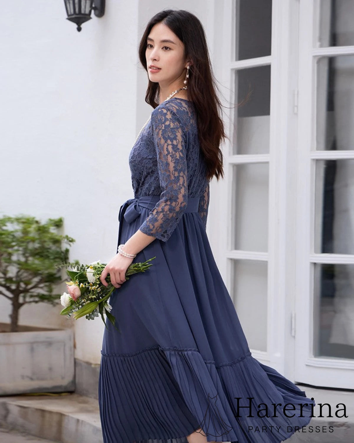 ダークブルーのレースシフォンドレスを着た女性が花束を持ち横向きで歩くシーン
