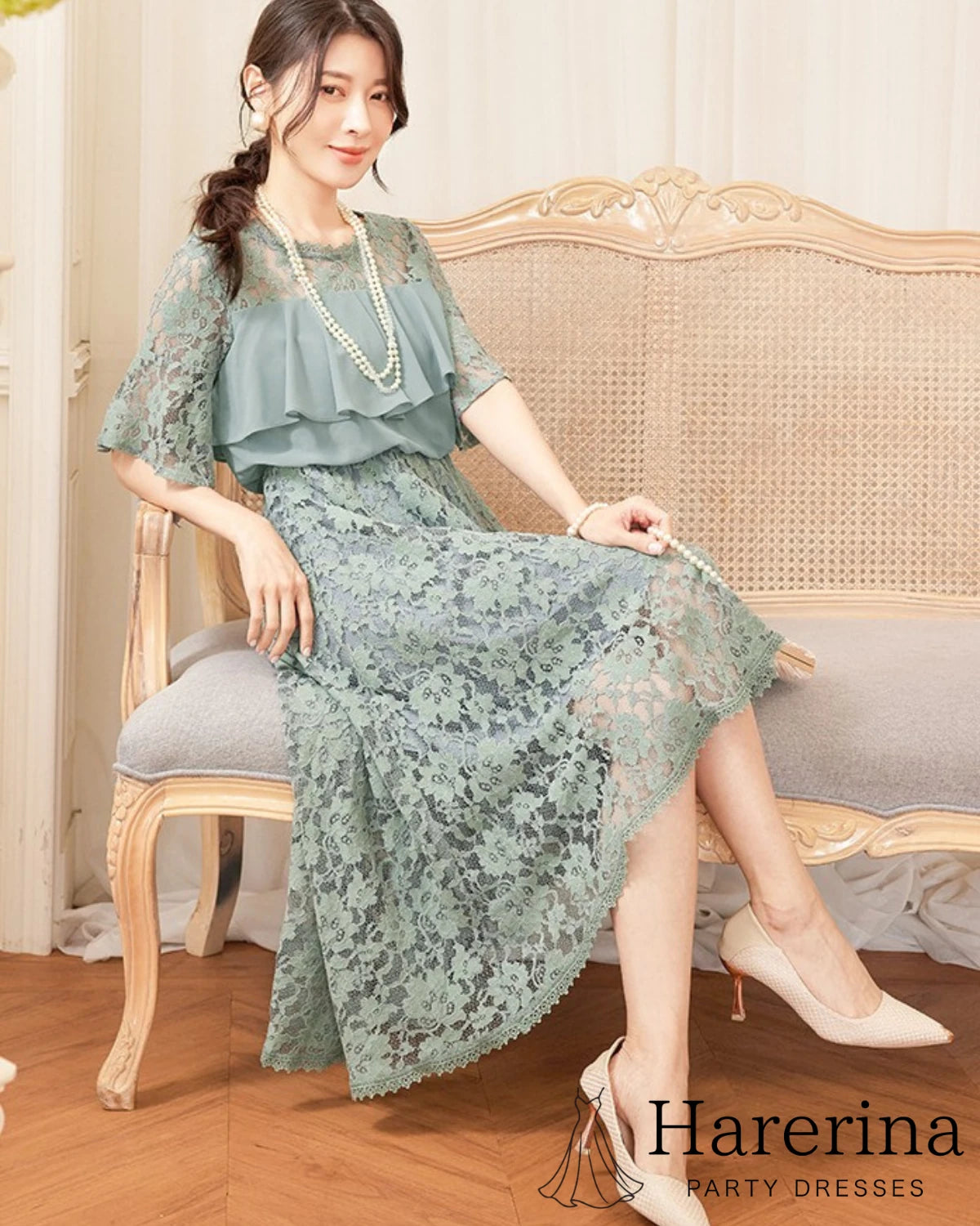 フリルレースが華やかなアシンメトリードレス（グレーブルー）を着た女性がソファに座り、柔らかなカラーの質感が伝わる姿
