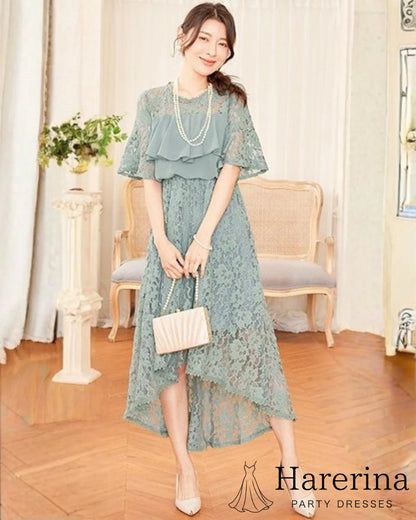 フリルレースが華やかなアシンメトリードレス（グレーブルー）を着た女性が上品に立ち、淡い色味が映えるシーン
