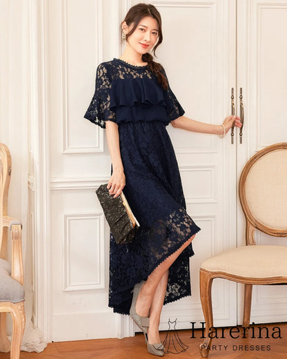フリルレースが華やかなアシンメトリードレス（ネイビー）を着た女性がドア横で上品にポーズを取っているシーン
