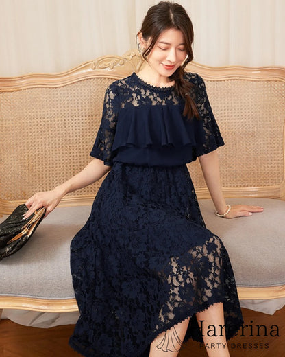 フリルレースが華やかなアシンメトリードレス（ネイビー）を着た女性がソファに座り、ディテールがよく見えるシーン
