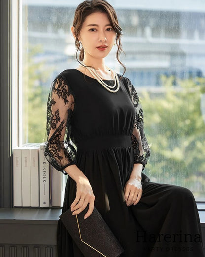 ブラックのレース袖プリーツワンピースを着た女性がクラッチバッグを持ちながら窓辺で座っている様子
