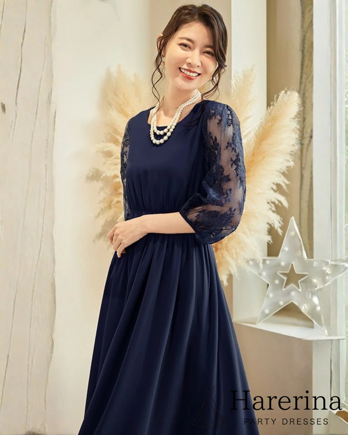 ネイビーのレース袖プリーツワンピースを着た女性が柔らかく微笑みながら立っている上半身カット
