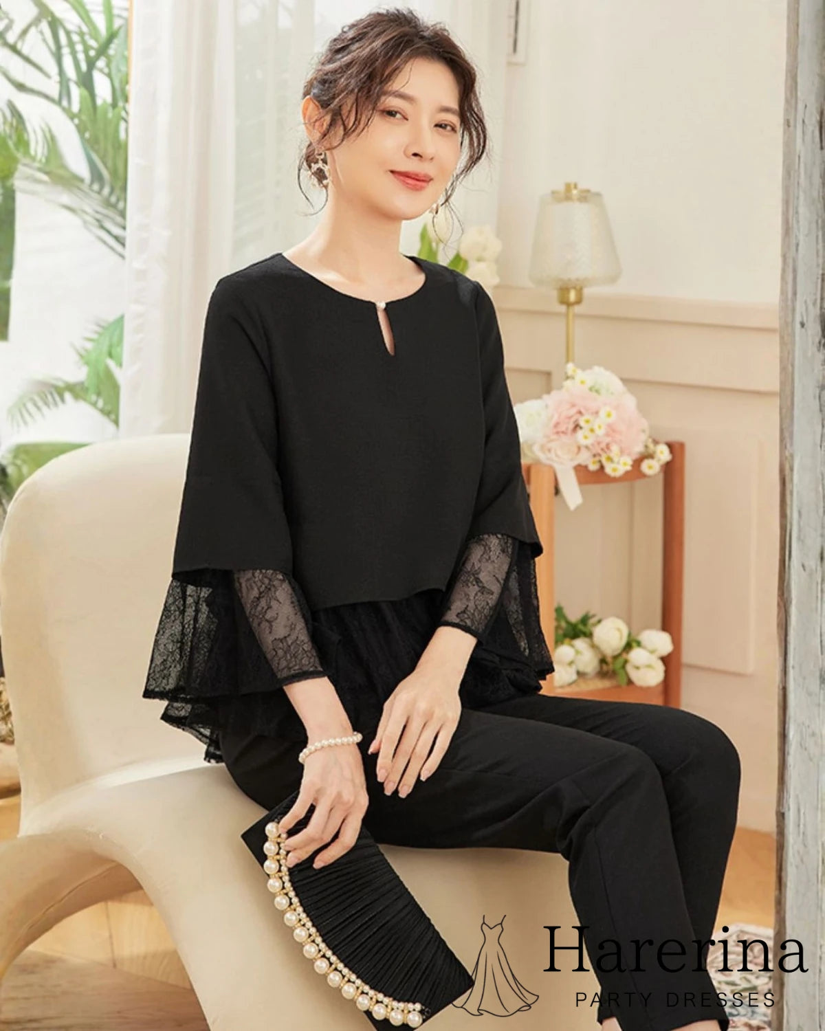 ブラックの体型カバーが叶うレース切替2点セットアップを着用したモデルが椅子に座り、袖レースの軽やかさが映える雰囲気のアップ画像。
