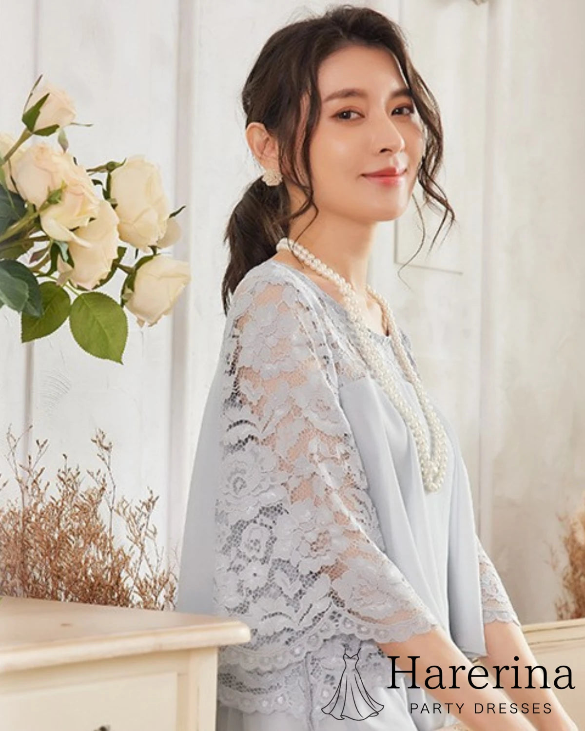 グレーのレーストップス×フレアワンピースを着たモデルの上半身アップ。繊細な花柄レース袖とパールネックレスが華やかで上品な印象を引き立てている。

