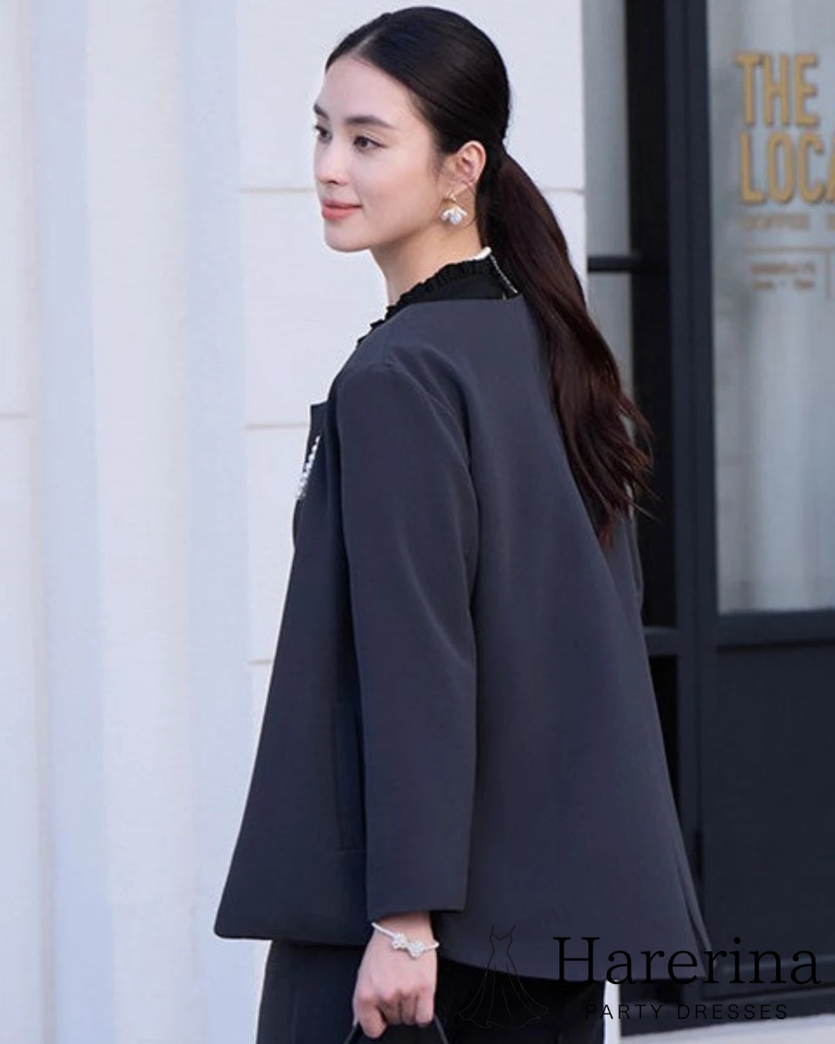 ダークネイビーのノーカラージャケットを着た女性モデルの後ろ姿。きれいなシルエットと上品な雰囲気を捉えたカット。

