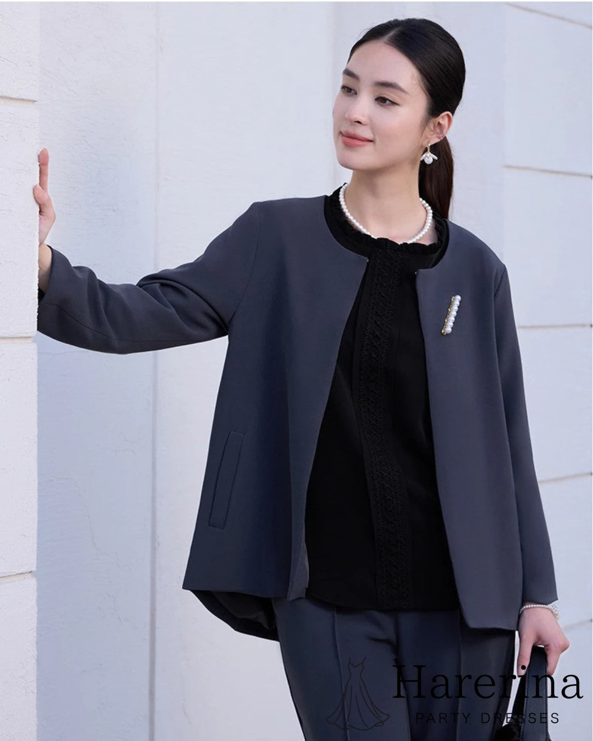 ノーカラージャケットとパンツのダークネイビーセットアップを着た女性モデルの上半身カット。黒トップスとパールアクセサリーを合わせた上品なスタイリング。

