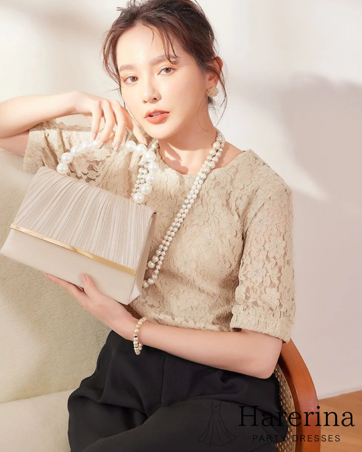 ベージュの華やかプリーツとパール持ち手が魅力のフォーマルクラッチバッグをモデルが手に持って撮影した画像。柔らかい色味と上品な印象が確認できる。
