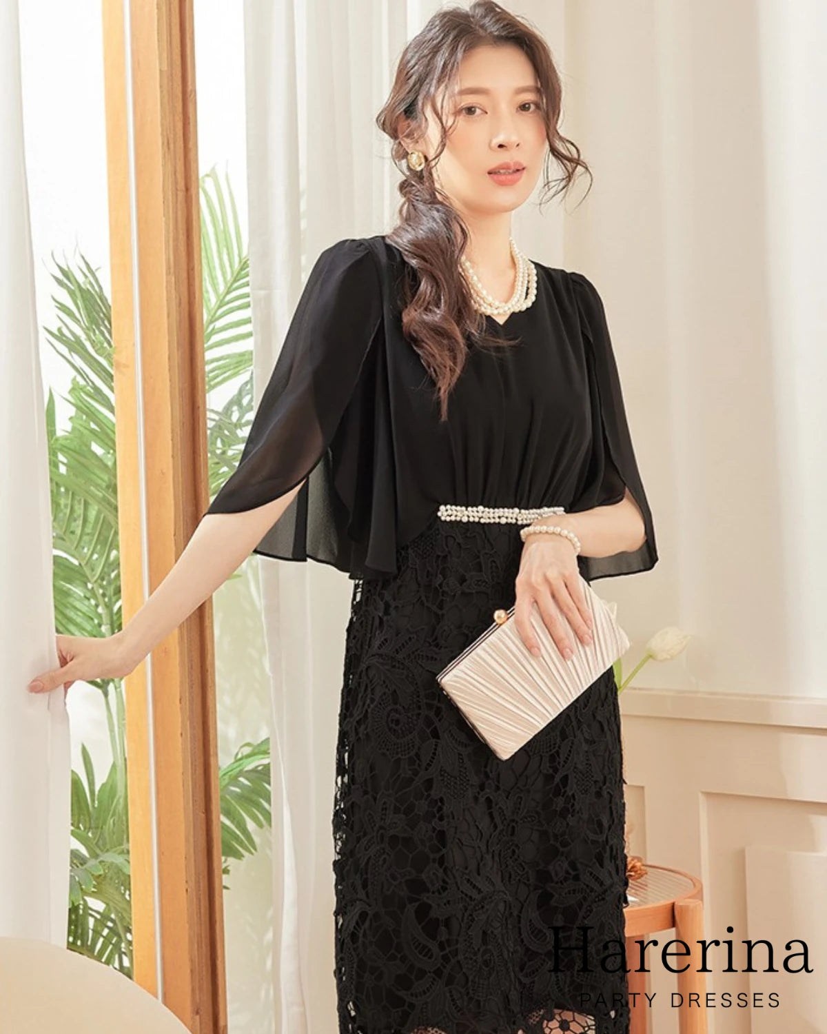 ブラックカラーのパールウエストマーク×膝丈レースドレスを着用した女性を正面から写した画像。パールネックレスとプリーツクラッチバッグを合わせた上品なコーディネート

