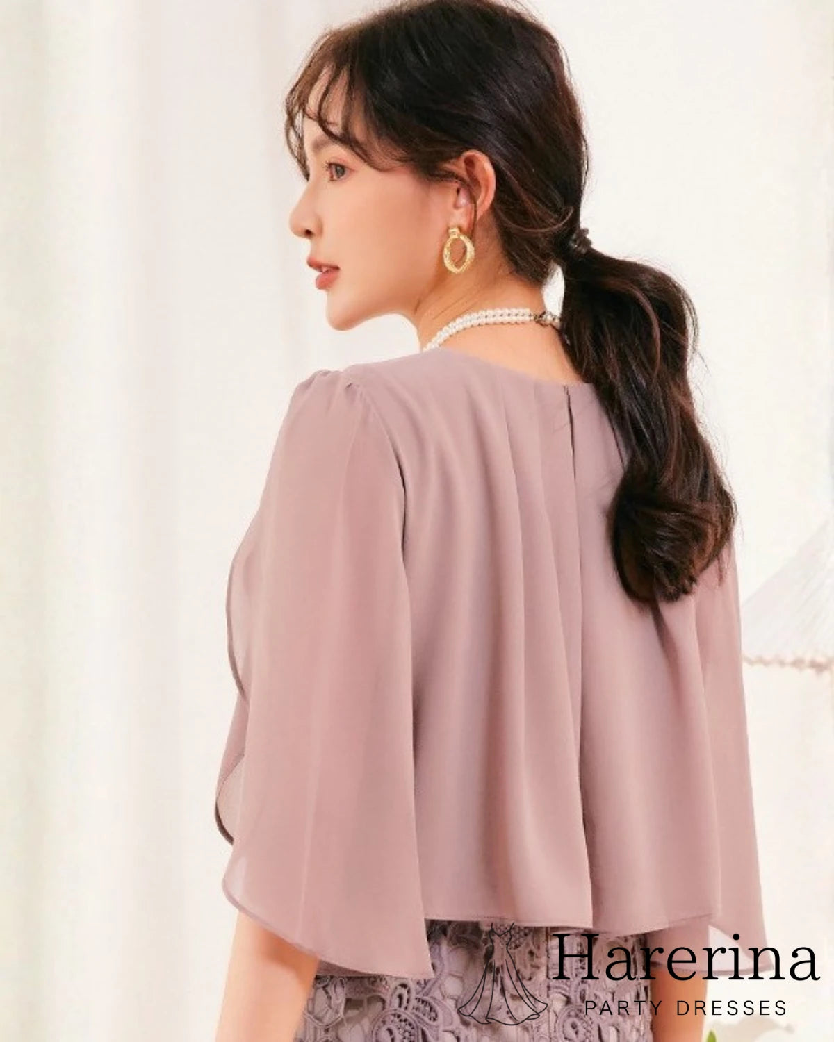 ローズグレーカラーのパールウエストマーク×膝丈レースドレスを着用した女性を背面から写した画像。シフォンのケープ風バックデザインが特徴
