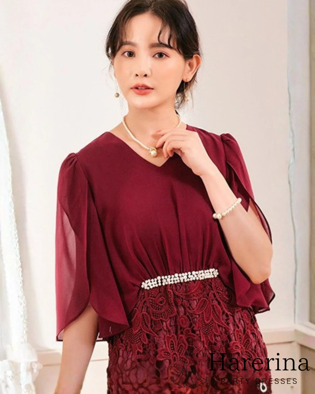 ワインレッドカラーのパールウエストマーク×膝丈レースドレスを着用した女性を正面から写した画像。シフォン袖とウエストのパール装飾が上品なデザイン
