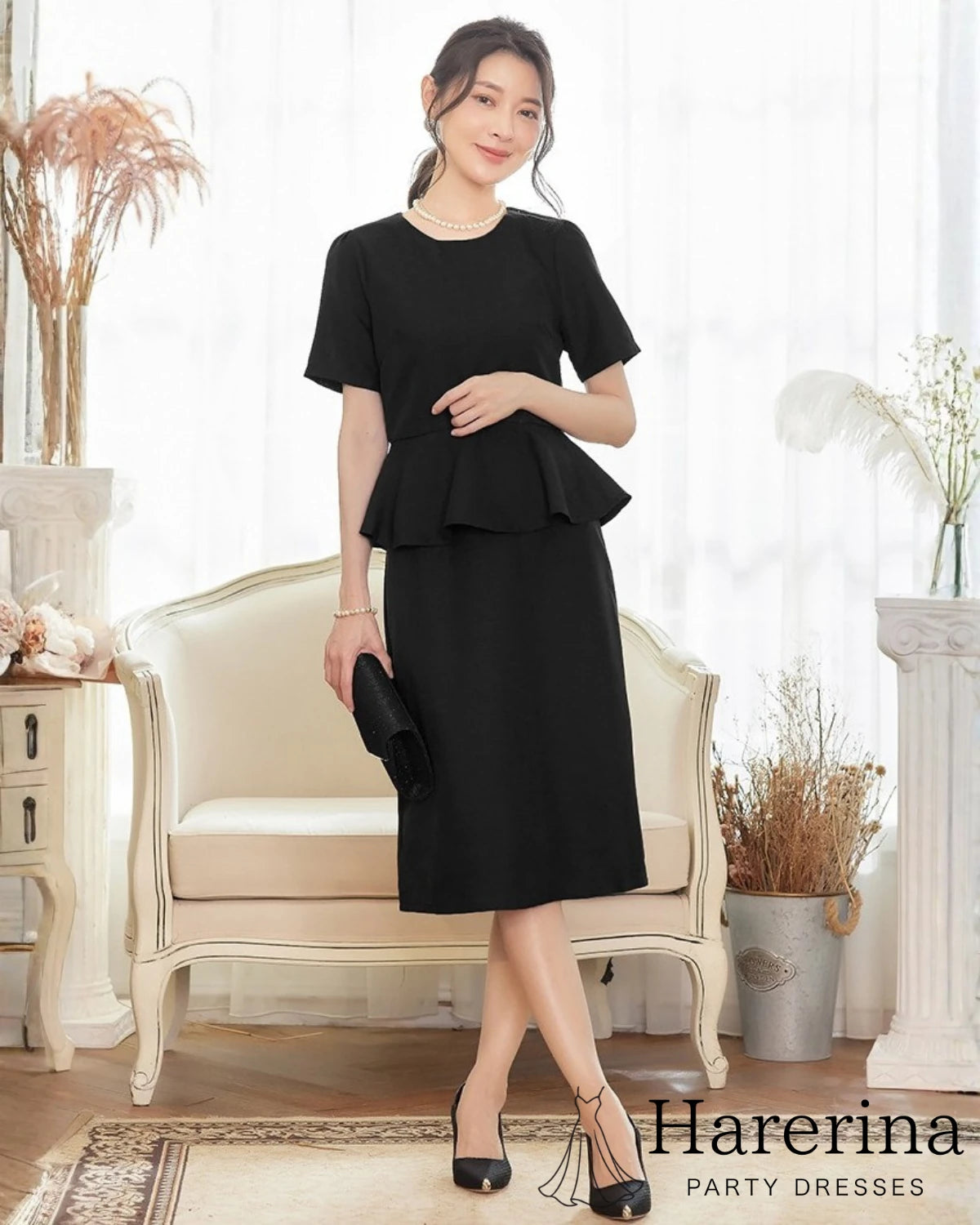 黒のペプラムワンピースを着た女性がクラッチバッグを持ち、上品な雰囲気で前向きに立つ全身コーディネート写真
