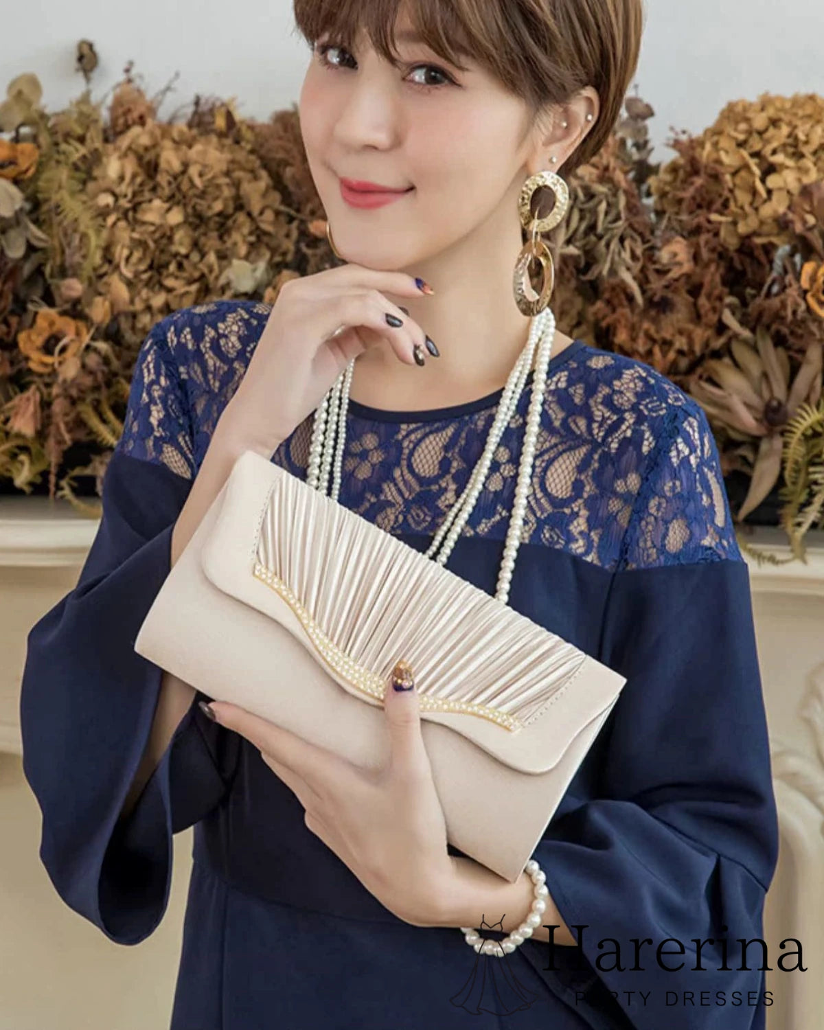 アプリコットのプリーツ×ラインストーンクラッチバッグを抱える女性のコーディネートアップ写真。
